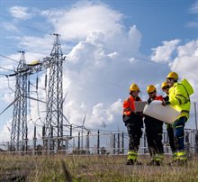 Team of workers discuss plans at a power plant site under blue sky with clouds during the day
