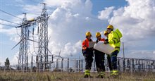 Team of workers discuss plans at a power plant site under blue sky with clouds during the day (1)